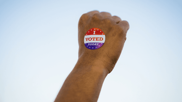 A hand with an "I Voted Today" sticker against a clear sky backdrop
