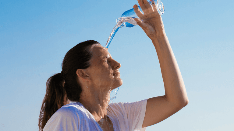 Woman pouring water over her head against a clear blue sky